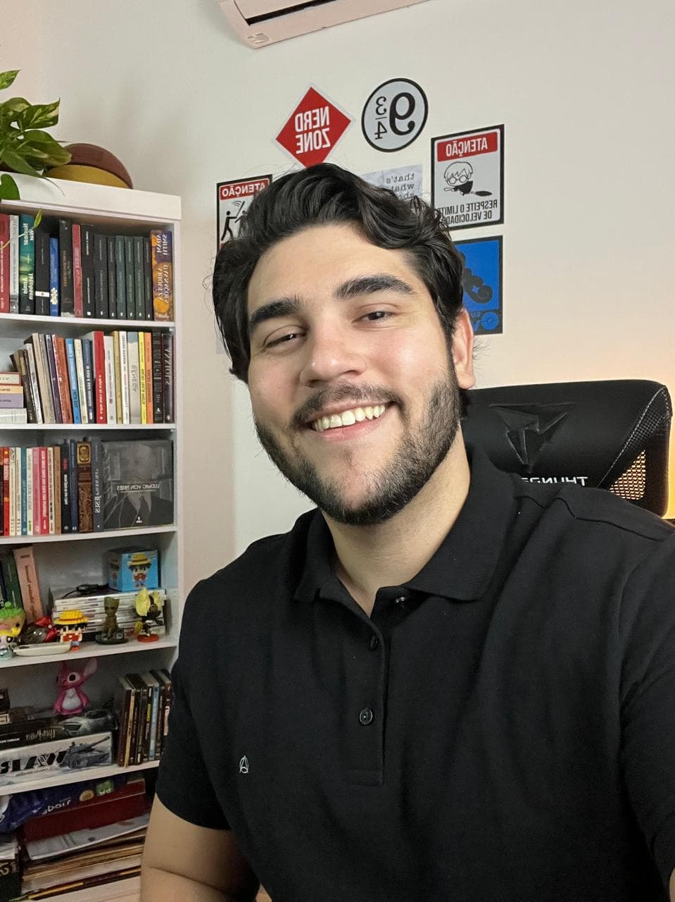 Vinícius, fundador do Olhar Estoico, sorrindo em frente à sua estante de livros